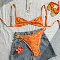 Bikini brésilien triangle orange imprimé posé à plat sur un short en jean, avec une fleur rose et des lunettes