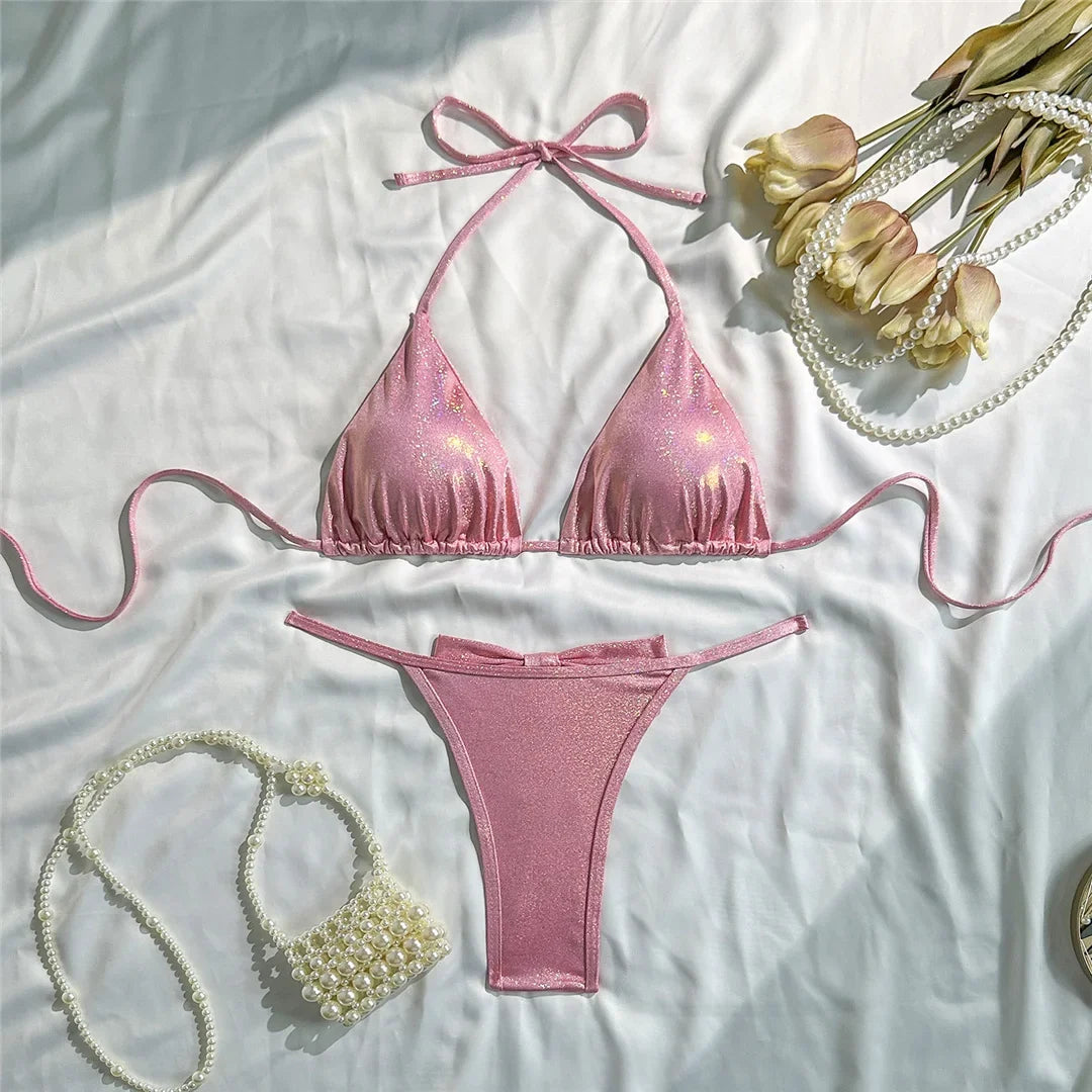 Bikini triangle tour de cou brillant rose posé à plat sur un tissu blanc, bretelles longues et bas à nœud