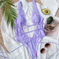Monokini décolleté plongeant découpe ventre violet posé à plat avec lacets déployés, près d'un avocat et de lunettes