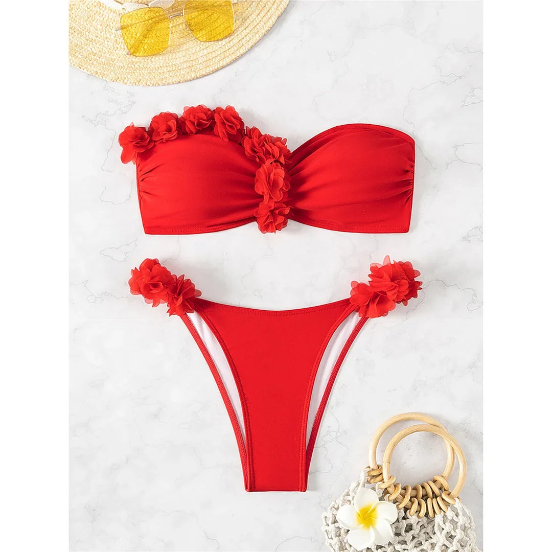 Bikini bandeau à fleurs en relief rouge posé à plat sur marbre blanc, avec un chapeau de paille et un sac en osier