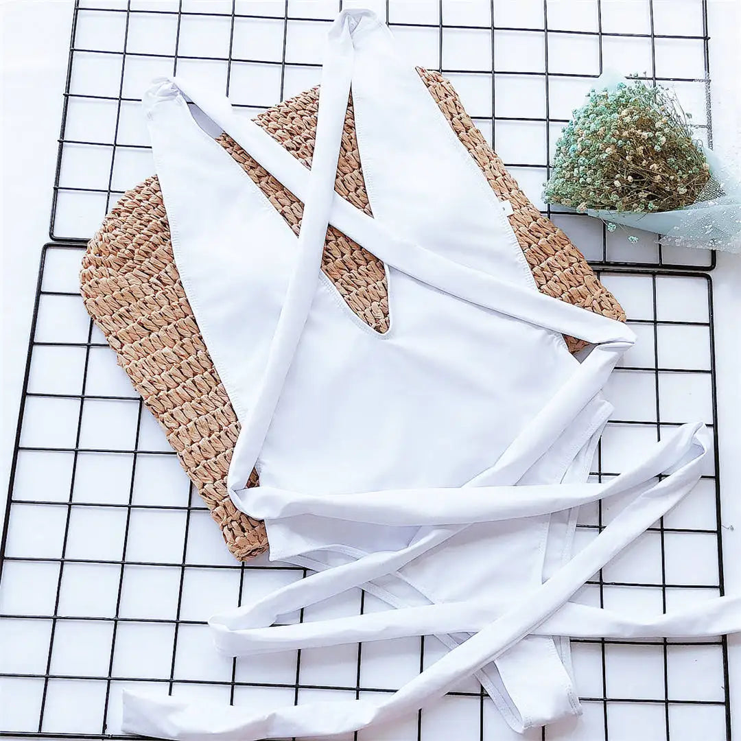 Maillot de bain une pièce triangle croisé blanc posé à plat sur une grille, lanières longues déployées