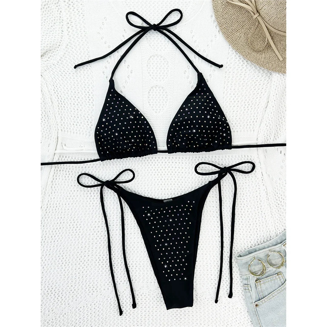 Bikini tour de cou à lanières noir orné de strass posé à plat sur une couverture blanche, avec un chapeau et un short en jean