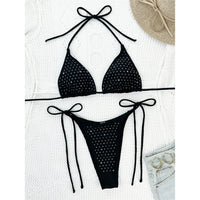 Bikini tour de cou à lanières noir orné de strass posé à plat sur une couverture blanche, avec un chapeau et un short en jean