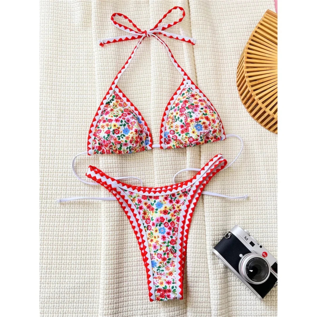 Bikini à petites fleurs sur fond blanc posé à plat sur un tapis en tissu, bordure rouge en zigzag et appareil photo à côté