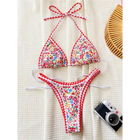 Bikini à petites fleurs sur fond blanc posé à plat sur un tapis en tissu, bordure rouge en zigzag et appareil photo à côté