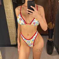Bikini brésilien string taille basse imprimé fleuri rouge porté de face devant un miroir en pied, triangle à liseré rouge