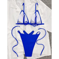 Bas de bikini bleu roi à lacets longs posé à plat sur une chemise blanche, vu de haut avec perles sur les côtés