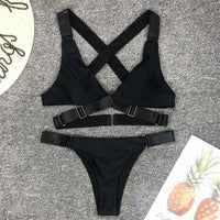 Bikini sans armatures croisé dans le dos noir posé à plat sur un tapis gris, sangles croisées et boucles réglables