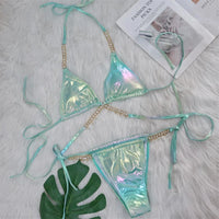 Bikini aspect simili cuir vert irisé posé à plat sur une fourrure blanche, avec une feuille verte