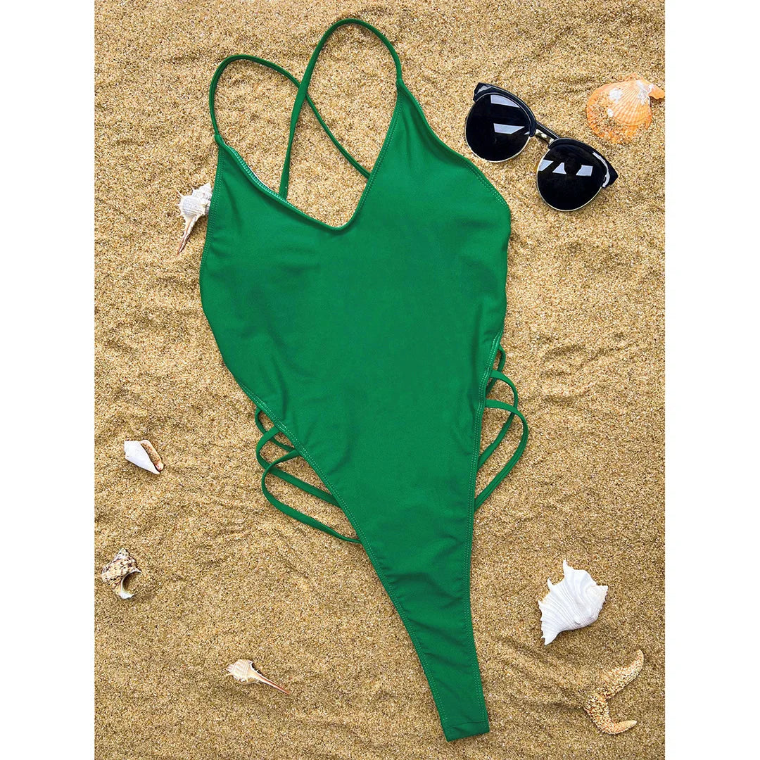 Maillot de bain une pièce vert posé à plat sur du sable, avec lunettes de soleil et coquillages autour
