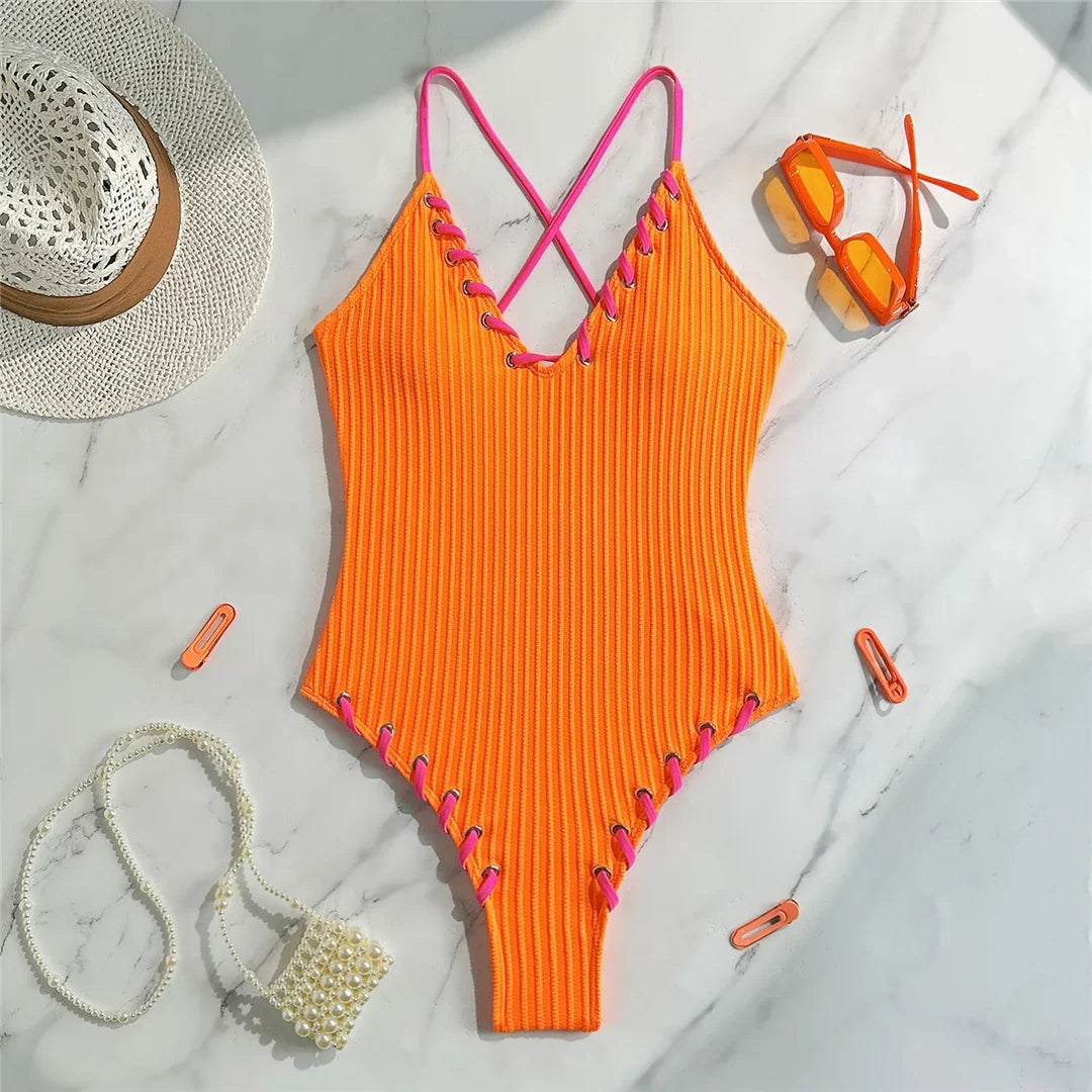 Maillot de bain une pièce côtelé orange posé à plat sur marbre, lacets rose fuchsia sur les bordures
