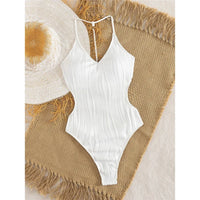 Maillot une pièce échancré texturé blanc à plat sur une natte en raphia, bretelles fines et détail perlé au décolleté