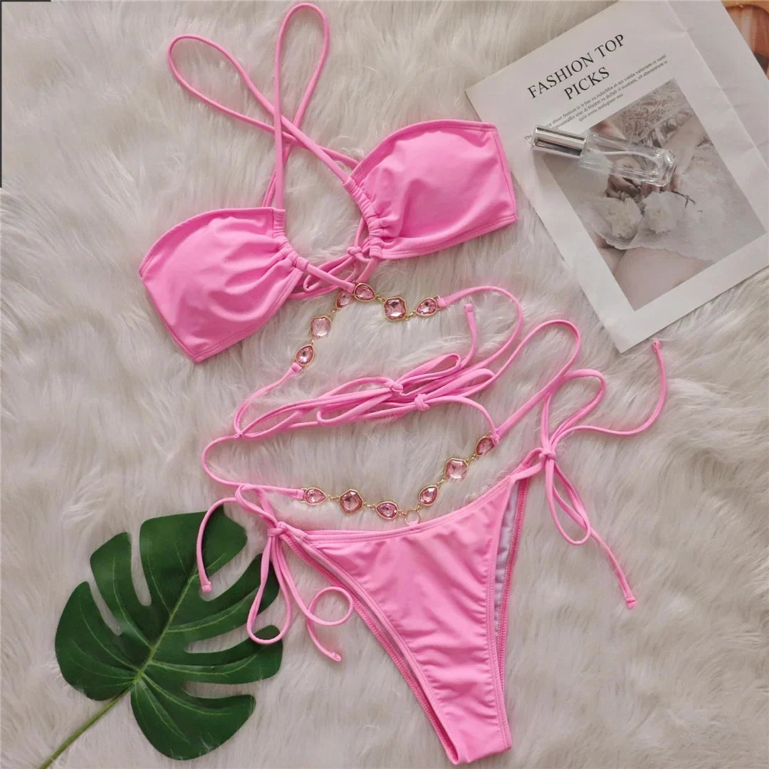 Bikini croisé sans armatures orné de strass rose posé à plat sur fourrure blanche, feuille verte et journal en décor