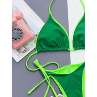 Gros plan sur le haut triangle vert foncé bordé de vert fluo, col halter et culotte nouée posés à plat à côté d'un téléphone