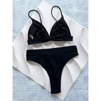 Bikini brésilien échancré taille haute noir vu à plat sur un motif blanc en vagues, haut croisé au centre et bretelles fines