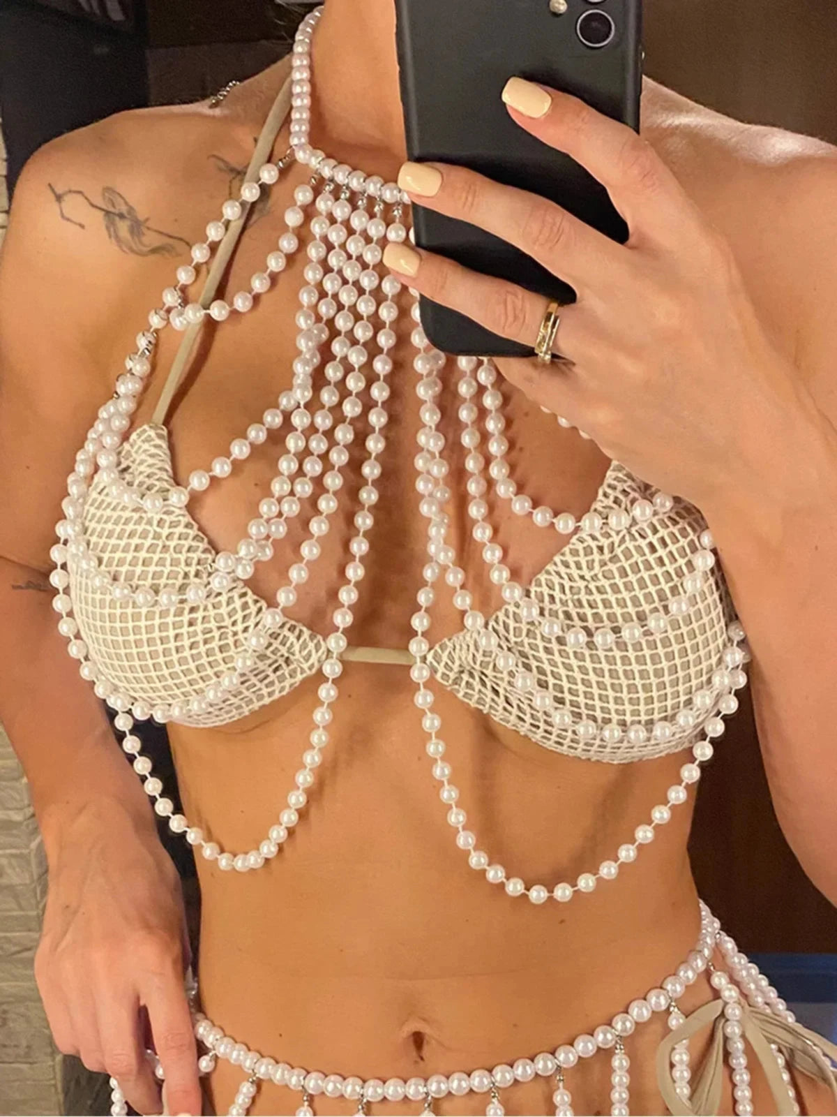 Haut de plage à perles ajouré tour de cou blanc posé à plat sur fond gris, avec collier de perles et lunettes orange