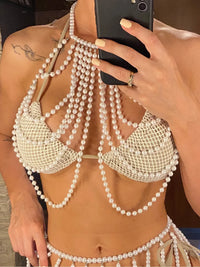 Haut de plage à perles ajouré tour de cou blanc posé à plat sur fond gris, avec collier de perles et lunettes orange