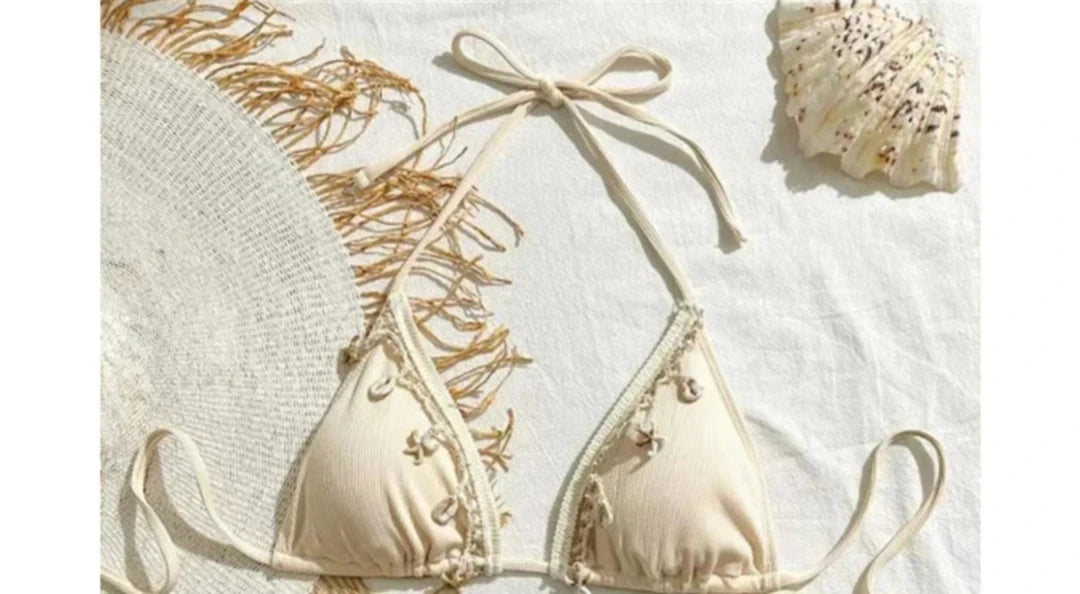 Gros plan sur le haut du bikini triangle à nœuds et breloques dorées sable