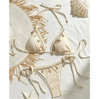 Bikini brésilien tour de cou patchwork à lanières marron clair posé à plat, teinte sable avec breloques dorées