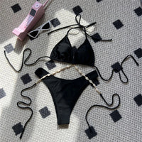 Bikini brésilien coquille noir posé à plat sur un tapis, triangle sans armatures et chaîne de coquilles dorées sur le bas