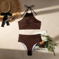 Bikini taille haute tour de cou texturé marron café posé à plat sur une table, avec chapeau de paille et livre à côté