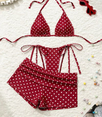 Maillot trois pièces à pois rouge posé à plat sur un tapis blanc, chapeau de paille en haut à gauche