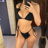 Bikini triangle noir orné de fleurs 3D et lanières nouées sur les côtés, porté de face devant un miroir