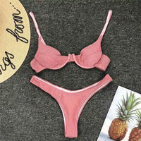 Bikini rose pailleté à armatures posé à plat sur un tapis gris, bas à liseré blanc, à côté d'un ananas