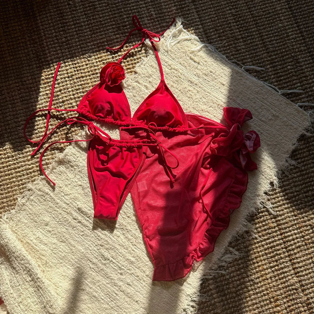 Maillot rouge à plat sur un tapis en fibres, haut à fleur en relief et bas à liens, pareo volanté posé à côté