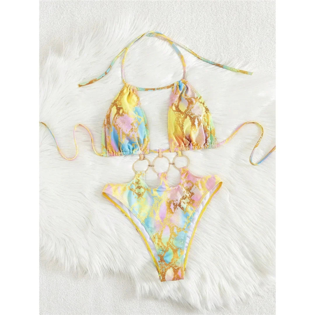 Maillot de bain tour de cou imprimé jaune pastel à anneaux dorés en bas du haut, lunettes jaunes posées à côté