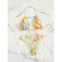 Maillot de bain tour de cou imprimé jaune pastel à anneaux dorés en bas du haut, lunettes jaunes posées à côté