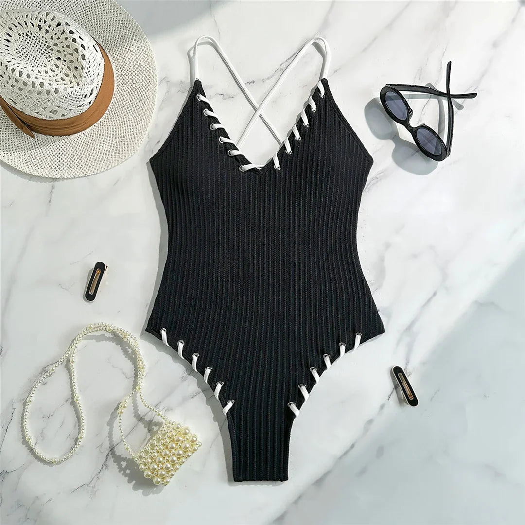 Maillot de bain une pièce côtelé noir posé à plat sur marbre, lacets blancs sur les bordures et bretelles croisées