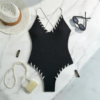 Maillot de bain une pièce côtelé noir posé à plat sur marbre, lacets blancs sur les bordures et bretelles croisées