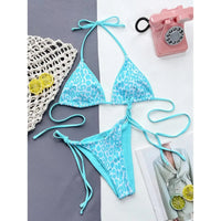 Bikini brésilien triangle imprimé léopard bleu clair posé à plat sur fond gris et bleu, téléphone rose et citrons