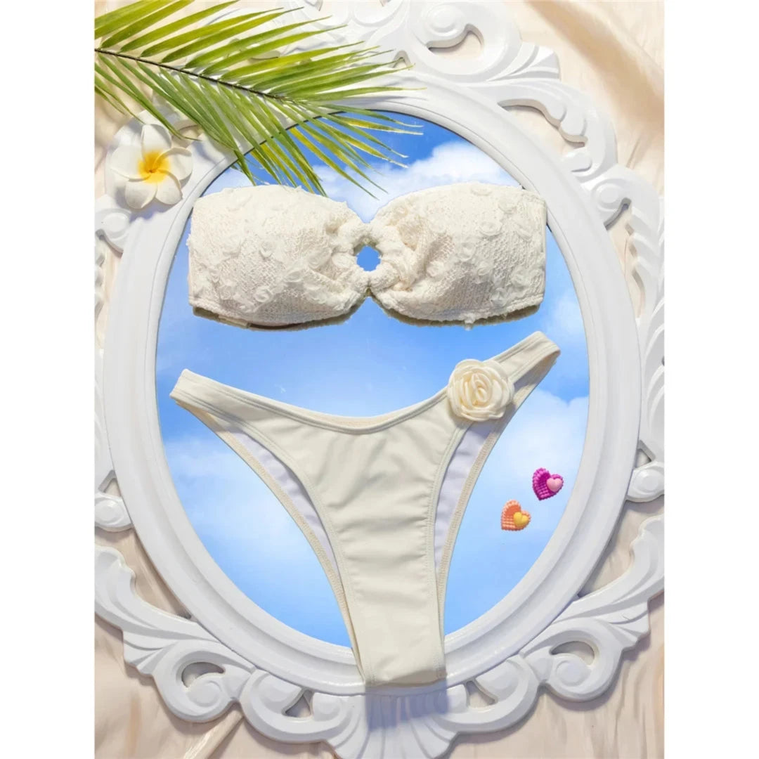 Bikini bandeau échancré à fleurs en relief blanc cassé posé à plat dans un cadre ovale blanc sur fond de ciel