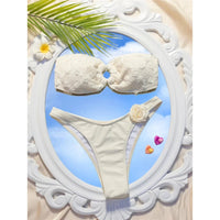 Bikini bandeau échancré à fleurs en relief blanc cassé posé à plat dans un cadre ovale blanc sur fond de ciel