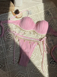 Bikini côtelé à armatures bords festonnés rose posé à plat sur une dentelle au soleil, perles sur les liens