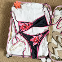 Bikini brésilien triangle imprimé fleuri noir et rose à plat dans une valise, fleurs rouges et liseré rose au crochet