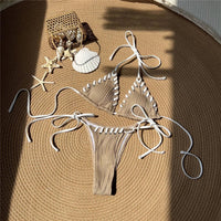Bikini tour de cou caramel posé à plat sur une natte ronde, brides blanches longues et coquillages autour
