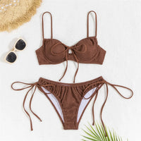 Bikini à armatures effet froissé marron café posé à plat sur un tapis blanc, bas noué, chapeau et lunettes