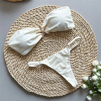 Bikini bandeau string échancré à étoile métallique beige posé à plat sur un tapis en osier, étoile dorée au centre