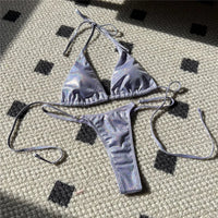Bikini brillant scintillant triangle taille basse violet posé à plat sur un tapis, triangle et culotte à liens latéraux