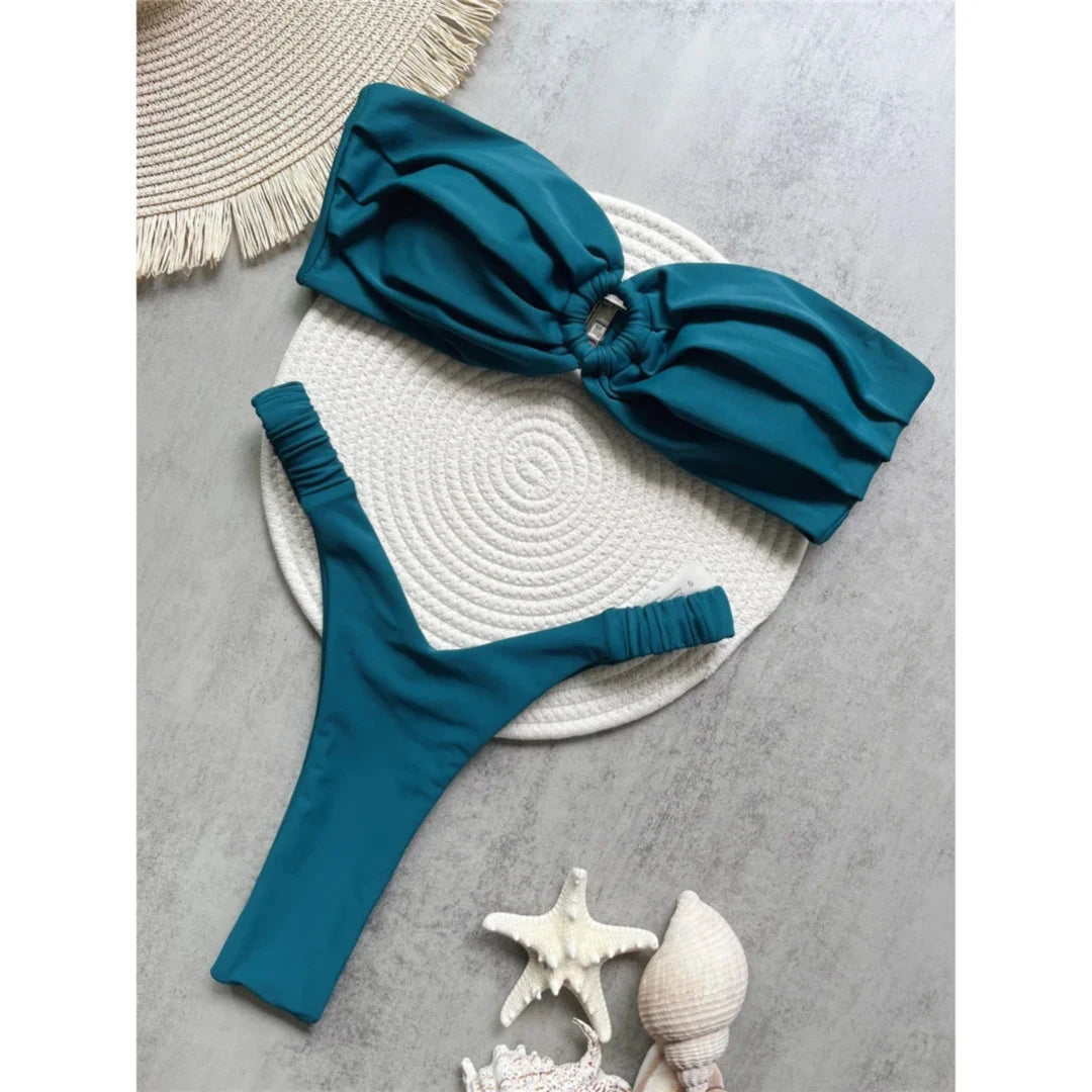 Bikini bandeau string texturé froissé vert foncé posé à plat sur un tapis rond blanc, bas à attaches latérales fines