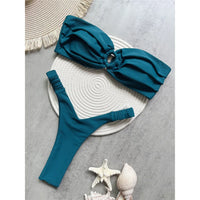 Bikini bandeau string texturé froissé vert foncé posé à plat sur un tapis rond blanc, bas à attaches latérales fines
