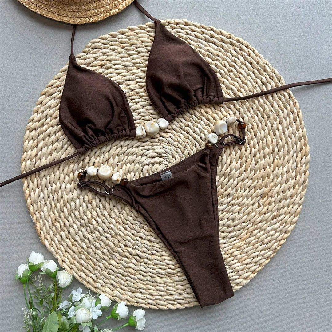 Bikini brillant tour de cou marron posé à plat sur un tapis en osier, perles nacrées le long des bretelles et du slip