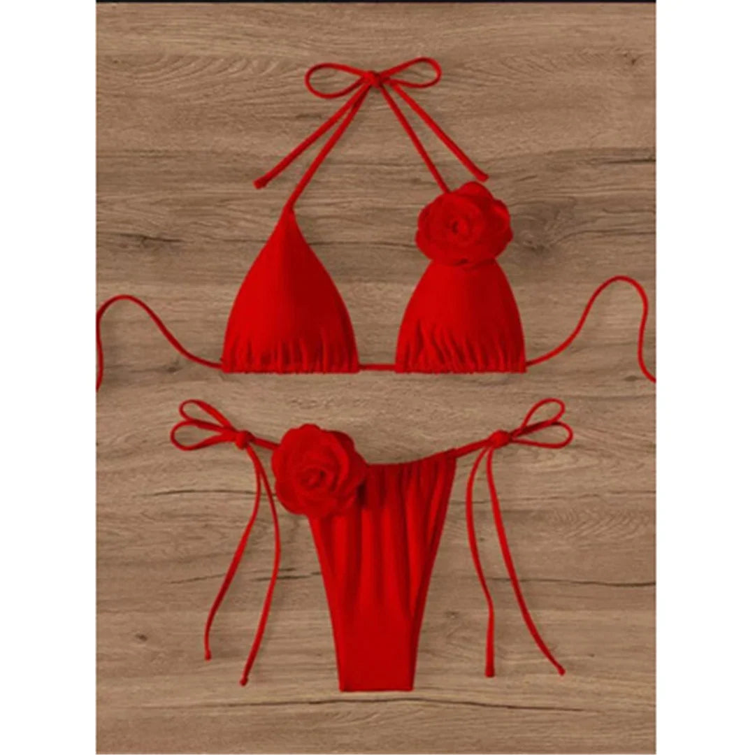 Bikini tour de cou à fleurs 3D et lanières rouge posé à plat sur fond bois, fleurs en relief sur le haut et sur le bas