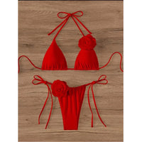 Bikini tour de cou à fleurs 3D et lanières rouge posé à plat sur fond bois, fleurs en relief sur le haut et sur le bas