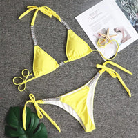 Bikini orné de strass brillants taille basse jaune posé à plat sur fond gris, bordure du bas blanche et strass