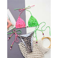 Bikini tour de cou à empiècements imprimé léopard posé à plat sur fond bicolore, haut vert et rose et bas léopard près d'un sac