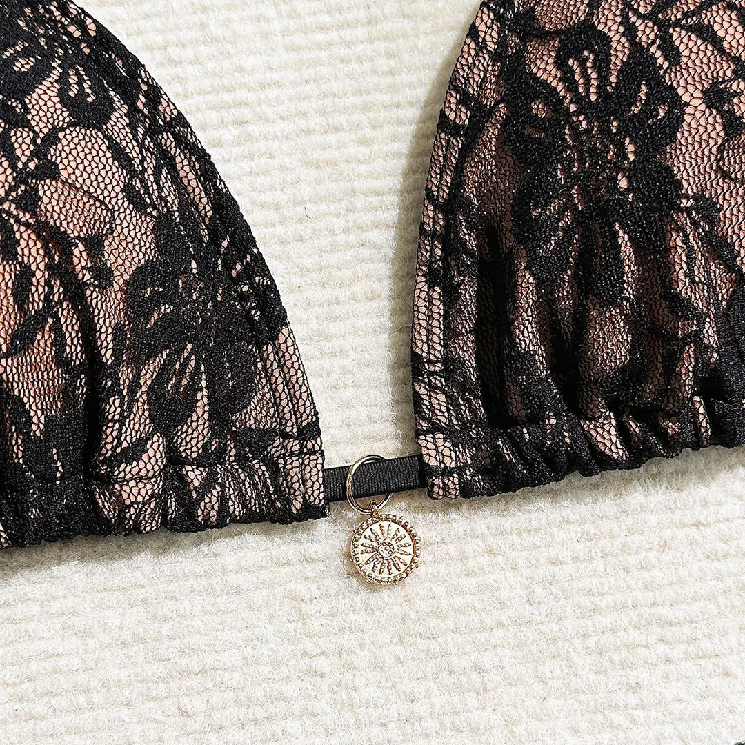 Gros plan sur le haut triangle noir en dentelle sur fond beige, avec le petit anneau doré au centre